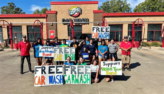 A group of students hold up signs advertising a ZIPS Fundraiser for Springdale Public School outside their local ZIPS Car Wash